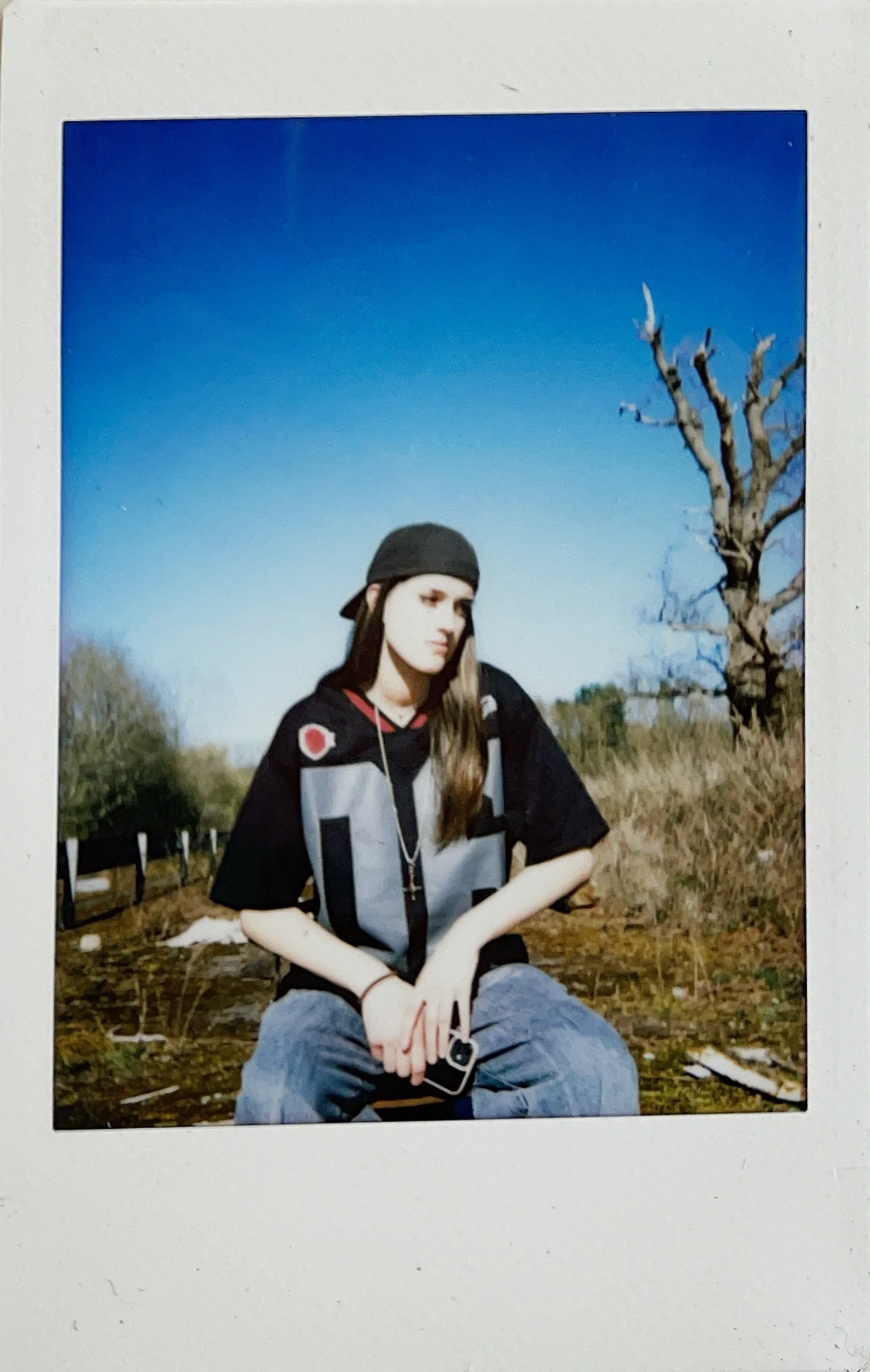 Polaroid portrait of a seated subject beneath bare trees