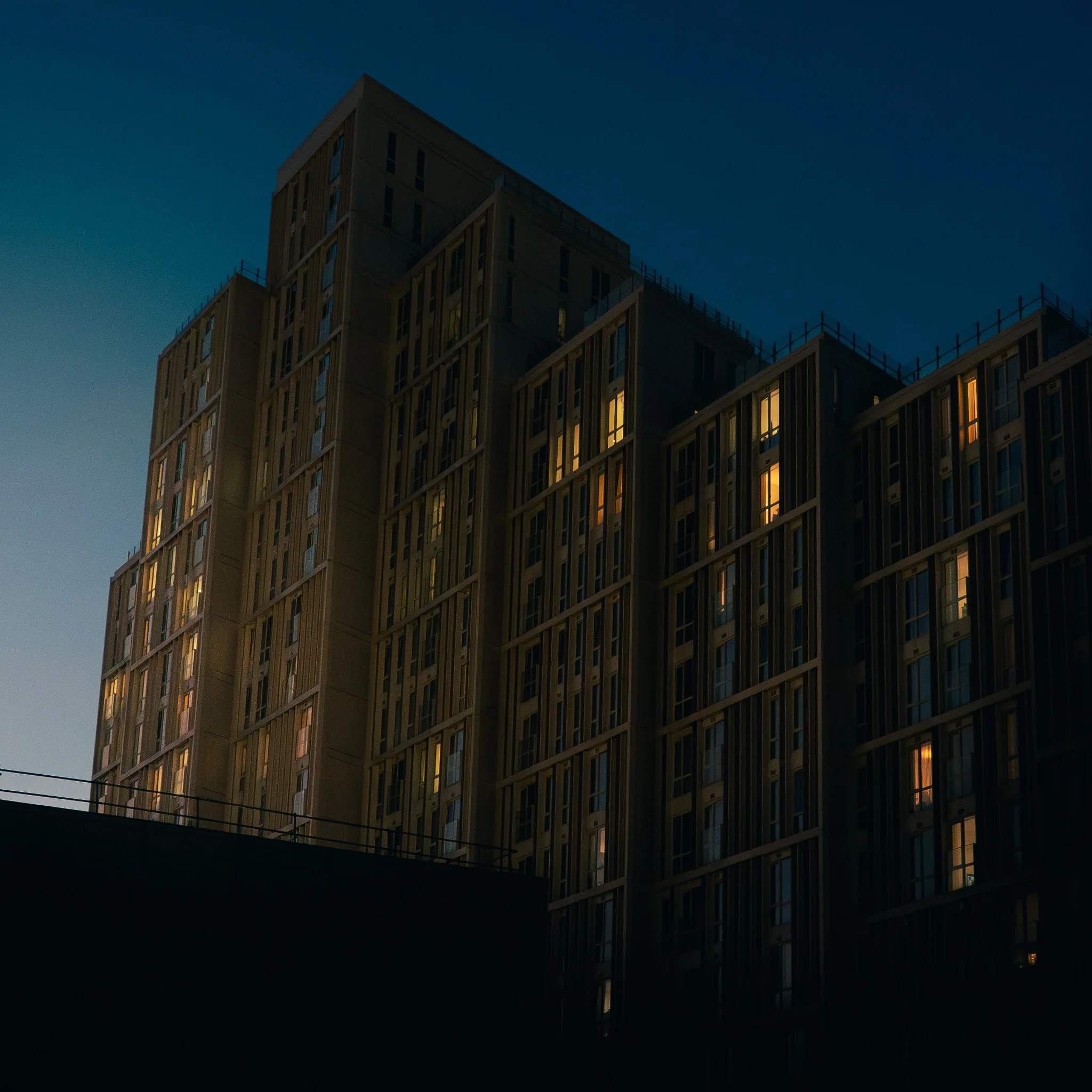 Tall residential building at blue hour with warm illuminated windows