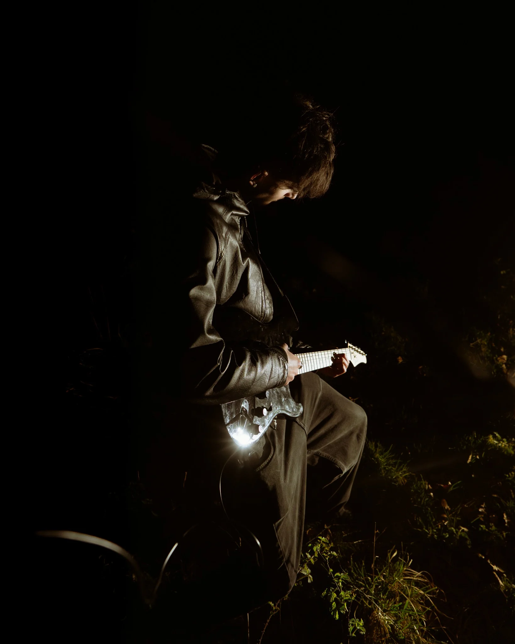 Guitarist seated in darkness with dramatic directional light